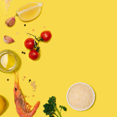Modern seafood minimal concept.  Flat lay, made of fresh organic pink prawn, olive oil, rice, tomato, garlic, parsley, lemon, himalayan salt, pepper against  yellow background. Creative copy space