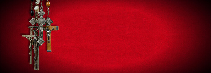 Close-up of a group of metal and wooden Crucifixes and Rosary Beads on Red Velvet Background with copy space.
