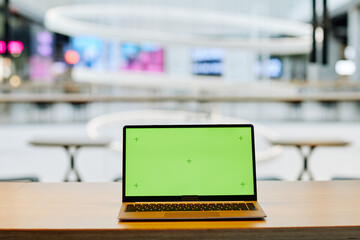 Background image of opened laptop with green screen chroma key on table in food court or cafe...