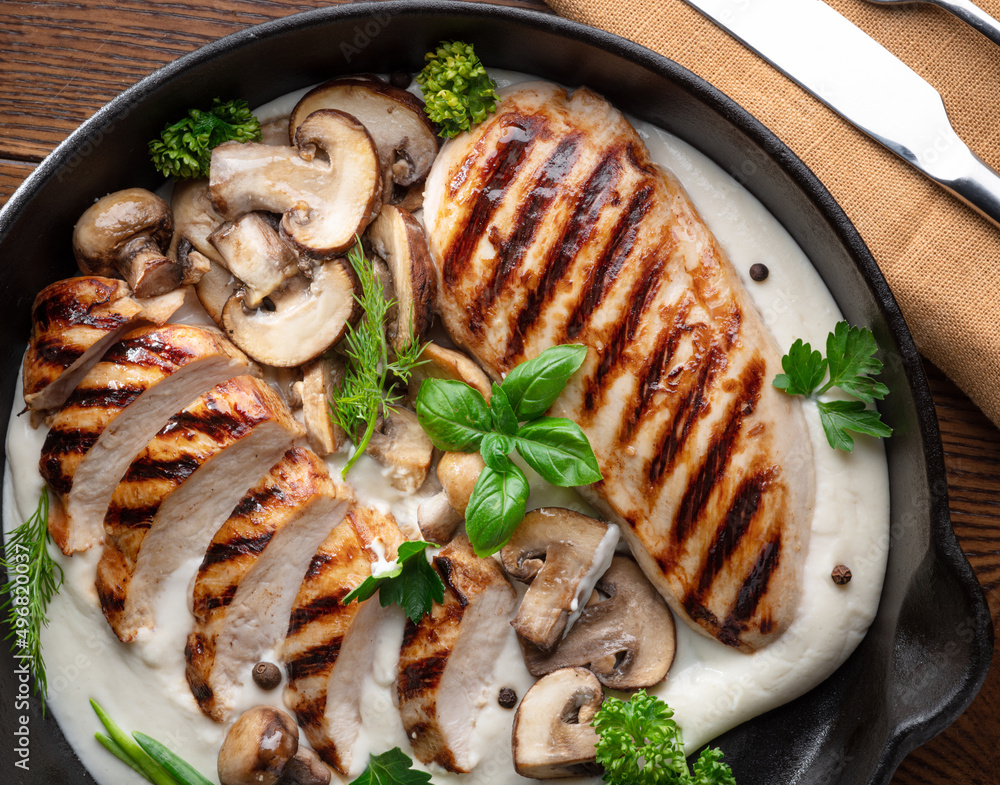 Wall mural Roasted chicken fillet and mushrooms with herb in the frying pan on the wooden table close-up.