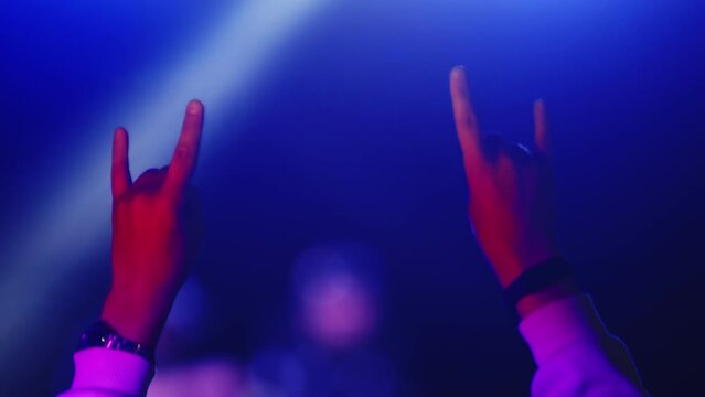 Hands of the jumping man move to beat of the music at concert and show rock gesture, closeup, back view. Slow motion. Concept party, a rock concert and fan support