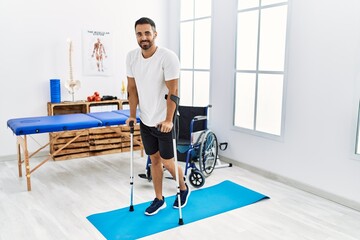 Young hispanic man patient having rehab session walking using crutches at clinic