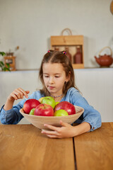 Fototapeta premium Little happy girl hold bowl with fruits in the kitchen at home, healthy child snack