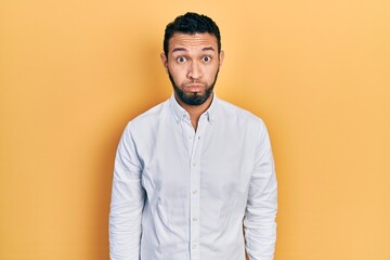 Hispanic man with beard wearing business shirt puffing cheeks with funny face. mouth inflated with...