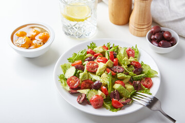 Salad with lettuce, cucumbers, tomatoes, olives and avocados in white plate on the table