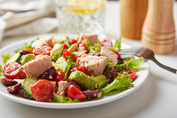 Salad with tuna, lettuce, cucumbers, tomatoes, olives and avocados in white plate on the table