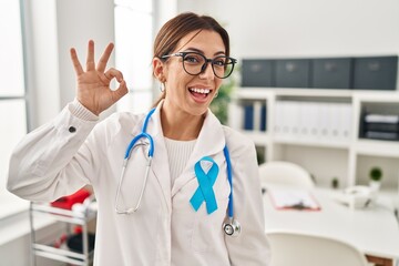 Young brunette doctor woman wearing stethoscope at the clinic smiling positive doing ok sign with hand and fingers. successful expression.