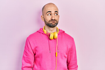 Young bald man wearing gym clothes and using headphones smiling looking to the side and staring away thinking.