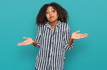 Young african american girl wearing casual clothes clueless and confused expression with arms and...