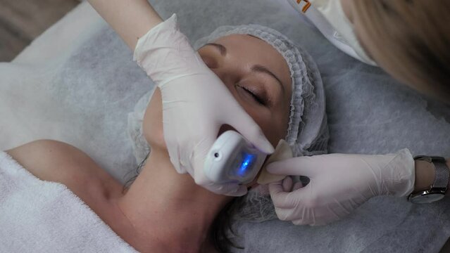 Cosmetologist cleans female face with hardware technique top view. Ultrasonic face cleaning in a beauty salon. Woman receives youth and skin care procedure