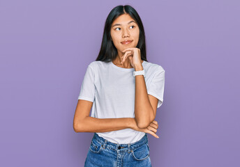 Beautiful young asian woman wearing casual white t shirt with hand on chin thinking about question, pensive expression. smiling and thoughtful face. doubt concept.