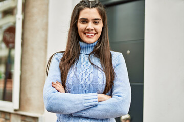 Young hispanic girl smiling happy with arms crossed gesture at the city