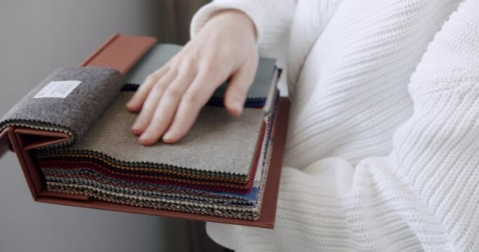 Close Up of female hands choosing fabric from color palette at textile showroom. Multicolor fabric texture background. Woman chooses color fabric in store. Textile store with colored fabric swatches