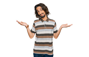 Young hispanic man wearing casual clothes clueless and confused expression with arms and hands...