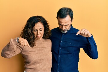 Middle age hispanic couple wearing casual clothes pointing down looking sad and upset, indicating...
