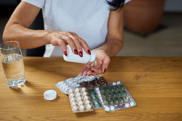 Mature sick woman having antibiotic, aspirin pills from bottle from flu