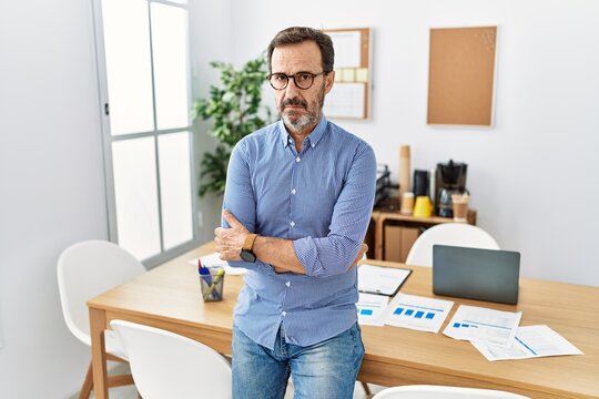 Middle age hispanic man with beard wearing business clothes at the office skeptic and nervous, disapproving expression on face with crossed arms. negative person.