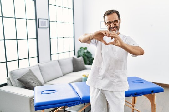 Middle age physiotherapy man working at home smiling in love showing heart symbol and shape with hands. romantic concept.