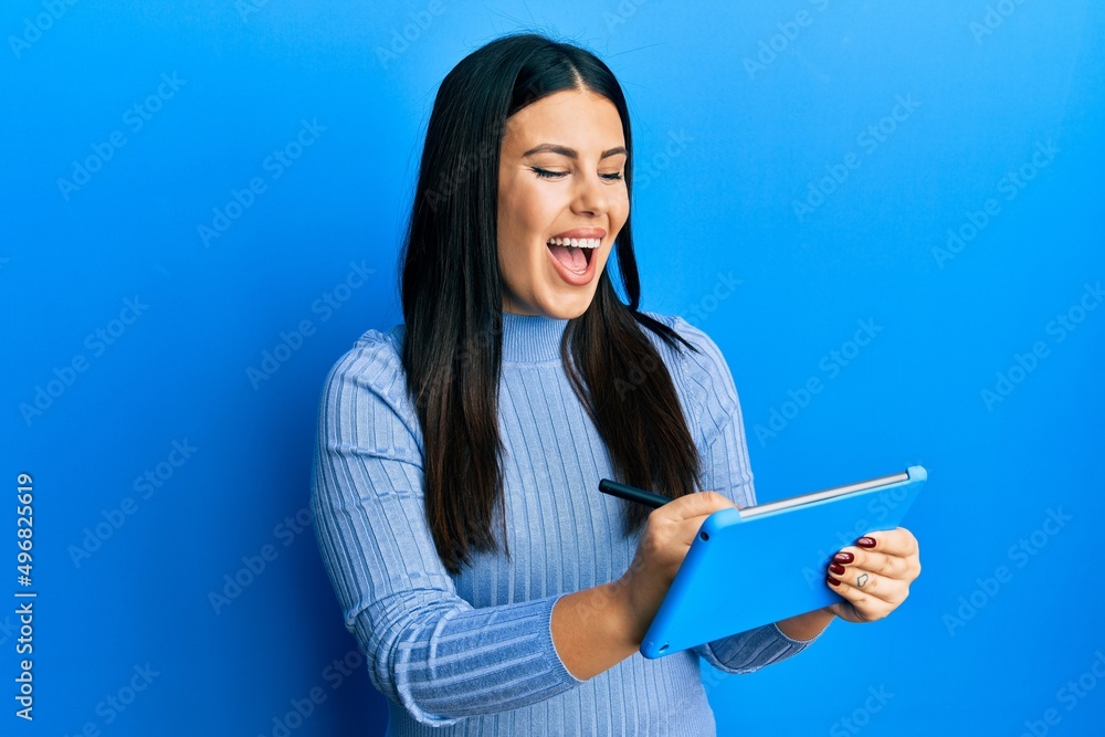 Wall mural Beautiful brunette woman using touchpad drawing on screen smiling and laughing hard out loud because funny crazy joke.