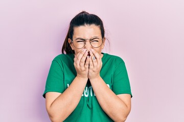 Young hispanic woman wearing volunteer t shirt laughing and embarrassed giggle covering mouth with...