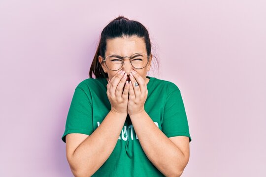 Young hispanic woman wearing volunteer t shirt laughing and embarrassed giggle covering mouth with hands, gossip and scandal concept