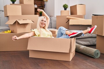 Fototapeta premium Young blonde woman smiling confident sitting in cardboard box at new home