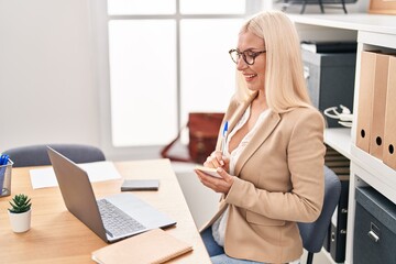 Obraz premium Young blonde woman business worker writing on reminder paper at office