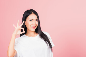 Obraz na płótnie Canvas Portrait Asian beautiful young woman standing, She made finger OK symbol sign to agree side away looking at camera, studio shot isolated on pink background, Thai female agree hand sign copy space
