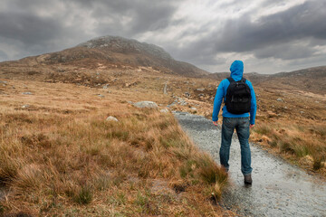 Fototapeta premium Male tourist walking towards Diamond hill, Connemara National Park, Ireland. Travel and hiking concept. Popular tourist area with stunning view. Irish nature landscape. Cloudy sky.