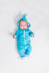 an asian baby in a blue warm children's suit lies on the bed and looks up. selective focus.
family at home
