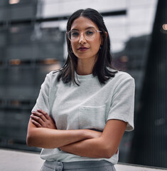 Determined to make it no matter the cost. Shot of an attractive young businesswoman standing alone in the office with her arms folded during a late shift.