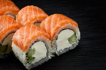 Philadelphia roll sushi with salmon, cucumber and cream cheese on black background for menu. Japanese food
