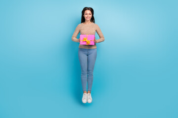 Full length body size view of attractive cheerful girl jumping holding festal giftbox isolated over bright blue color background