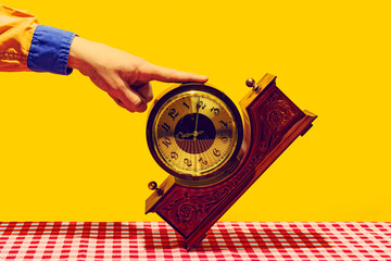 Retro things, pop art photography. Female hand touching vintage clock isolated on bright yellow background. Vintage, retro fashion style
