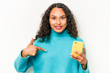 Young hispanic woman holding mobile phone isolated on white background person pointing by hand to a shirt copy space, proud and confident