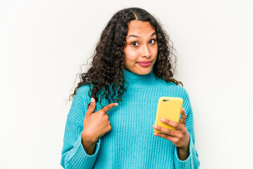 Young hispanic woman holding mobile phone isolated on white background pointing with finger at you as if inviting come closer.