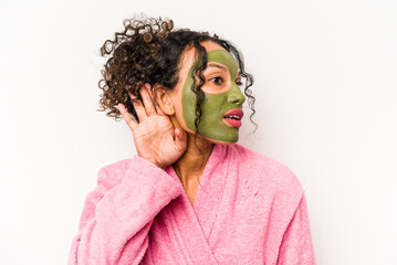Young hispanic woman wearing a facial mask isolated on white background trying to listening a gossip.
