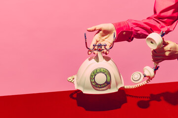 Pop art photography. Retro objects, gadgets. Female hand holding handset of vintage phone isolated on pink and red background. Vintage, retro fashion style