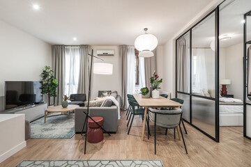 Living room with a wooden dining table, a gray three-seater sofa, balconies facing the street, oak flooring and a bedroom with a glass and metal wall