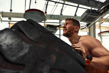 Fototapeta na wymiar Strongman, bodybuilding, sport, fitness and people concept - young man doing tire flip at training in gym