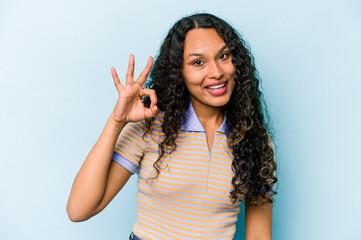 Young hispanic woman isolated on blue background cheerful and confident showing ok gesture.