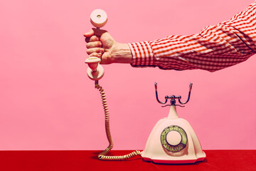 Pop art photography. Retro objects, gadgets. Female hand holding handset of vintage phone isolated on pink and red background. Vintage, retro fashion style