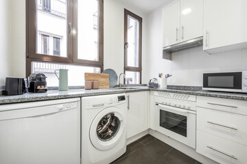 White kitchen with matching appliances, gray granite countertops and small countertop appliances, windows above the countertop and dark gray stoneware floors