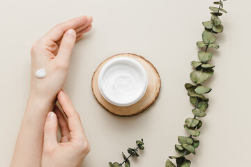Obraz na płótnie Canvas Woman applies cream on her hands, bottle with cream and eucalyptus leaves top view. Hands care, nourishing cream for soft skin