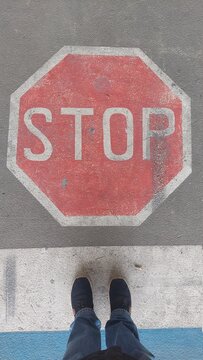 2 Füße in Jeans stehen still vor auf der Straße aufgemaltem Stopp-Schilod