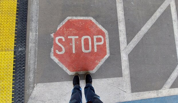 2 Füße in Jeans stehen still vor auf der Straße aufgemaltem Stopp-Schilod