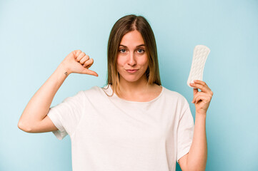 Young caucasian woman holding sanitary napkin isolated on blue background feels proud and self confident, example to follow.