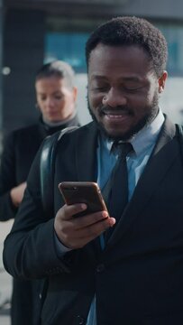 Portrait of an African American Businessman in a Suit Standing on a Street with Pedestrians. He's Using a Smartphone. He Looks Successful. Video Footage with Vertical Screen Orientation 9:16.