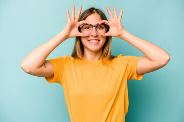 Young caucasian woman isolated on blue background showing okay sign over eyes