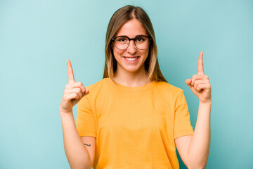 Young caucasian woman isolated on blue background indicates with both fore fingers up showing a...